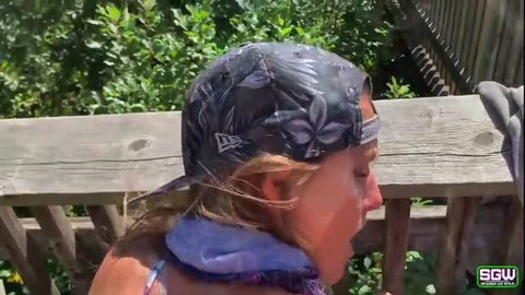 Blonde in baseball cap and bikini top reacts on public boardwalk
