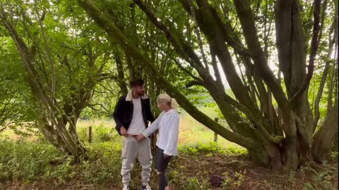 Couple standing in forest holding hands, clothed casual wear