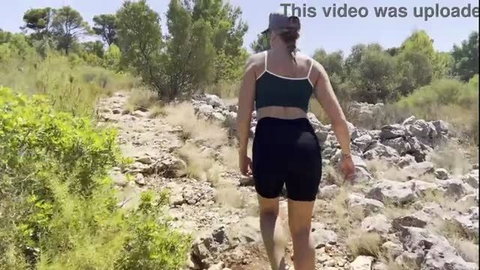 Curvy woman in black sports bra and shorts hiking on rocky trail