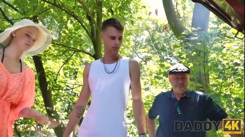 Blonde teen in orange dress with older man in forest scene