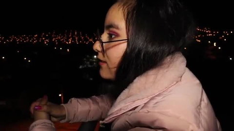 Young woman in pink puffer jacket at night with city lights
