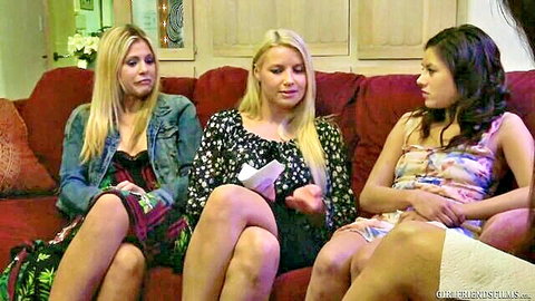 Three sexy clothed blonde and brunette young women sitting closely on red couch