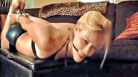 Blonde in black leather lingerie, bound with ropes and ball gag in BDSM pose