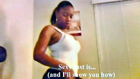 Curvy black woman in tight white tank top poses seductively with hands on hips