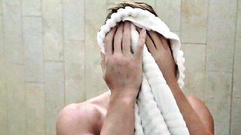 Naked muscular man covering face with towel in steamy bathroom