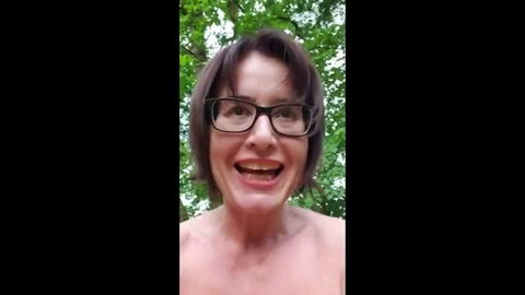 Mature woman with short brown hair and glasses topless outdoors