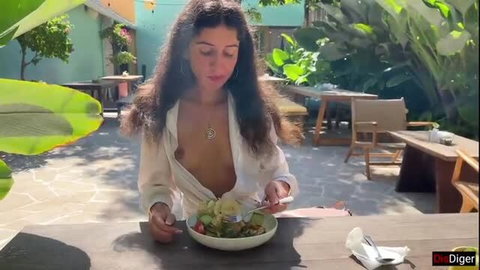 Brunette woman eats salad topless in public cafe