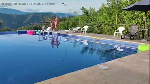 Two nude men standing poolside at a nudist camp overlooking mountains