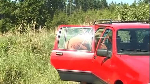 Redhead woman in red car with open doors in forest setting