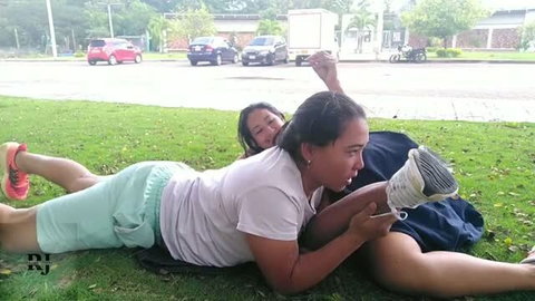 Couple making out on grass in park, woman on top, daytime public setting