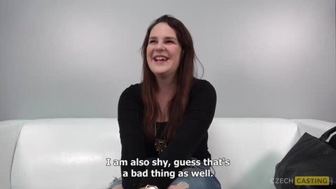 Michaela smiling on casting couch, long brown hair, black top