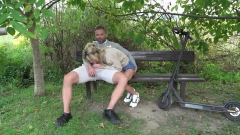 Blonde MILF cuddling with man on park bench next to electric scooter