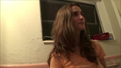 Molly Jane in orange top, long brown hair, indoor setting