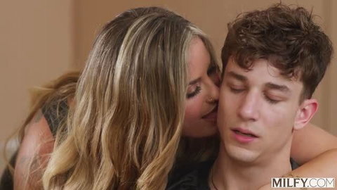 Mature blonde woman seductively kisses young man's neck