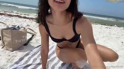 Woman in black bikini posing on beach towel with ocean view