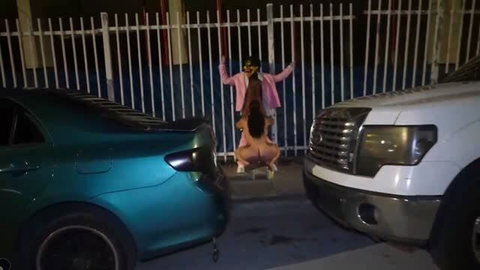Clown in pink jacket outdoors fucks a naked woman between parked cars