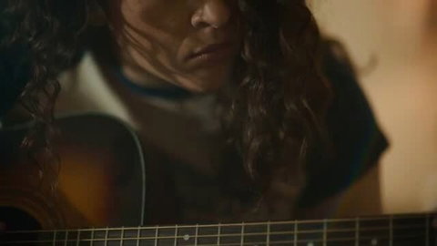 August Skye playing guitar in soft light, close-up face and acoustic