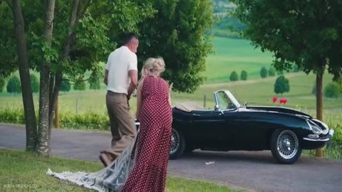 Candee Licious in red polka dot dress with older man outdoors by classic convertible