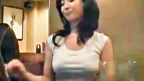 Asian woman in low-cut white tank top, smiling while holding hand at table