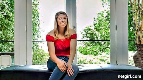 Blonde Caucasian woman in red off-shoulder top and jeans sitting and smiling