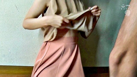 Asian woman lifting beige top to expose midriff in pink skirt, teasing with man nearby