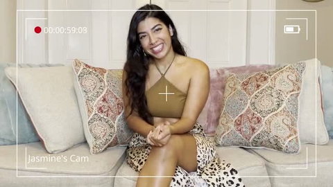 Jasmine Sherni sitting on couch in halter top and skirt, smiling