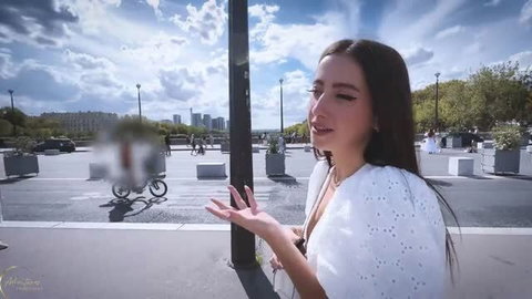 Li Moon in white eyelet top posing outdoors with blurred bystander blur