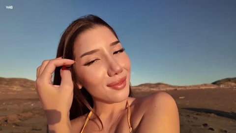 Layla Scarlett in yellow bikini, winking on sunny beach