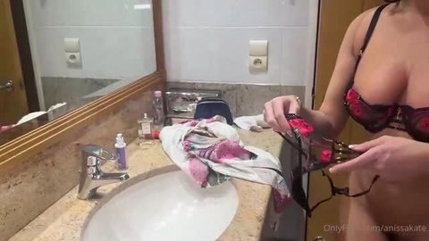 Anissa Kate in red lingerie holding leopard print bra in hotel bathroom