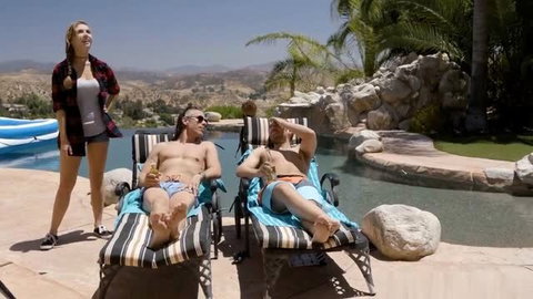 Lena Paul in plaid shirt stands by pool with two shirtless men on lounge chairs