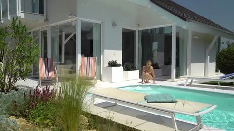 Alexa Flexy sits poolside in white bikini bottom, natural light, outdoor villa