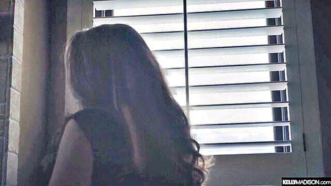 Brunette woman in tight top gazes seductively through window blinds