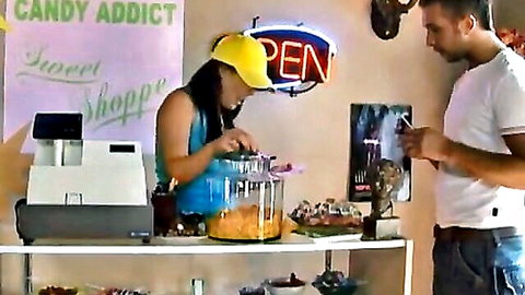 Petite Asian woman in tank top scoops candy in shop with male customer