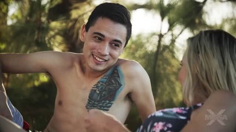 Smiling shirtless man with ship tattoo talks to blonde woman outdoors