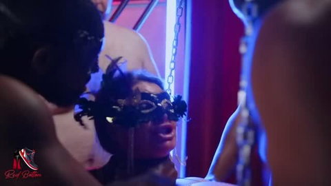 August Heat in black mask with feathers, surrounded by multiple men in red neon BDSM scene