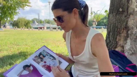 Gina Gerson reading photo album outdoors in white tank top