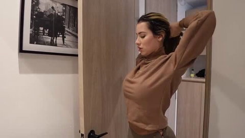 Ambar Prada in brown turtleneck, hands behind head, side profile