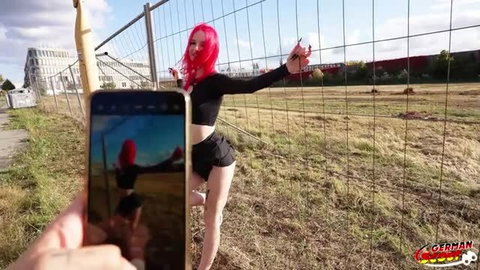 Redhead teen in black crop top and shorts posing outdoors by fence