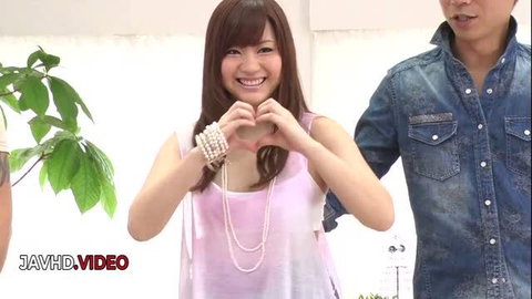 Mayuka Akimoto smiling and making heart gesture in pink top with two men