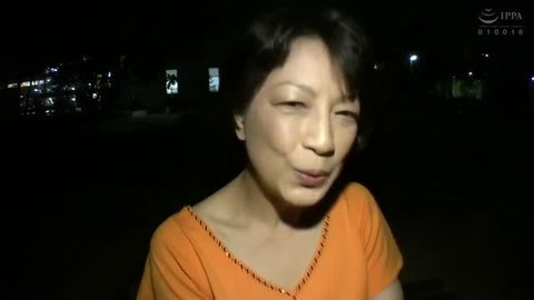 Mature Japanese woman in orange top, embarrassed expression, night scene
