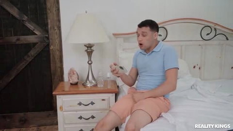 Man in blue shirt and pink shorts sitting on bed holding remote