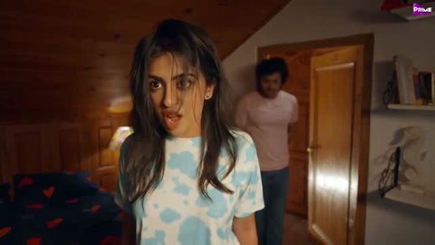 Woman in tie-dye shirt with shocked expression in bedroom scene
