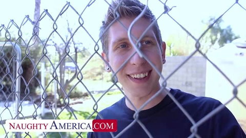 Johnny Castle smiling behind chain link fence in Naughty America scene