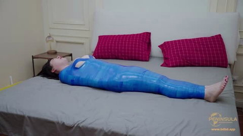 Woman fully encased in blue plastic wrap bondage on bed