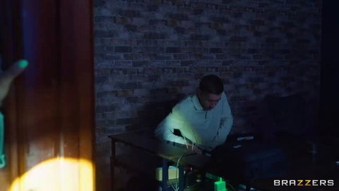 Skinny guy in white hoodie working on laptop in dark room
