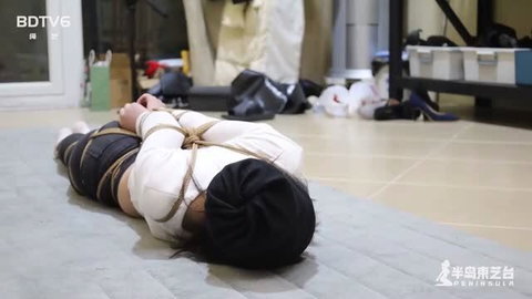 Asian woman bound with ropes in shibari style, wearing white top and black head covering