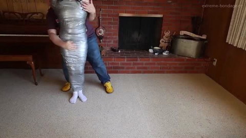 Mummification bondage with duct tape, fully wrapped submissive held by dominant partner