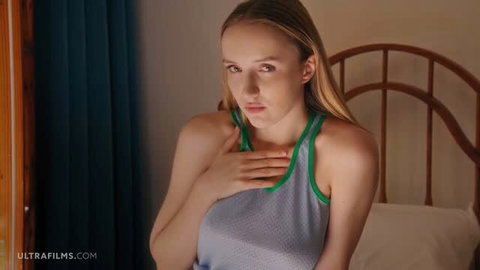Blonde teen in sheer tank top, hand on chest, softcore bedroom scene