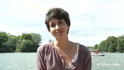 Short-haired woman in sheer blouse by lake, softcore tease