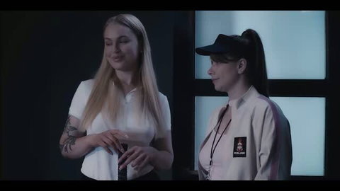 Two women in uniform shirts standing close together, one blonde in white polo, one brunette in cap